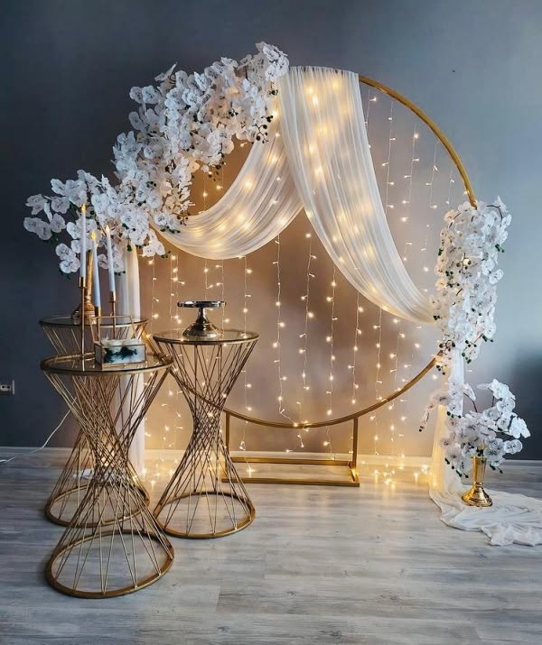 Cercle doré drapé de tulle blanc, rideau de lumières et guirlandes d'orchidées blanches, avec chandeliers et tables dorées