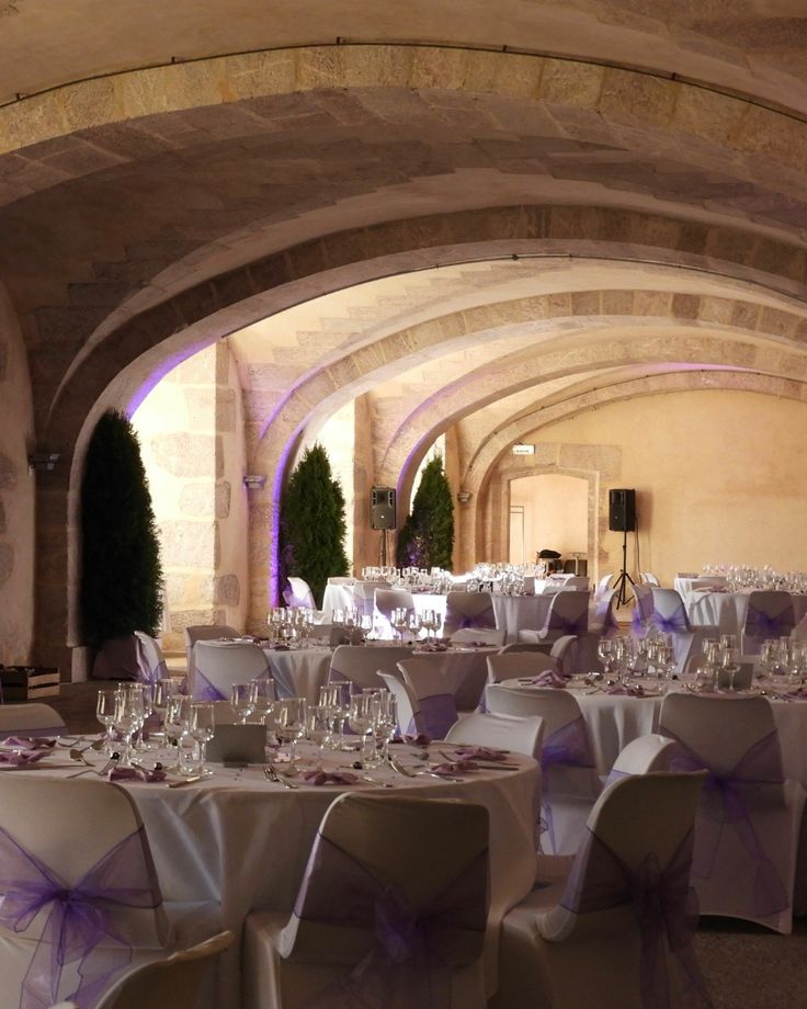 Salle voûtée en pierre dressée pour une réception privée avec chaises habillées de mauve